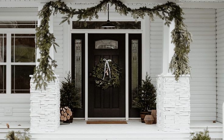 the front door of a white house with wreaths and pine cones hanging from it