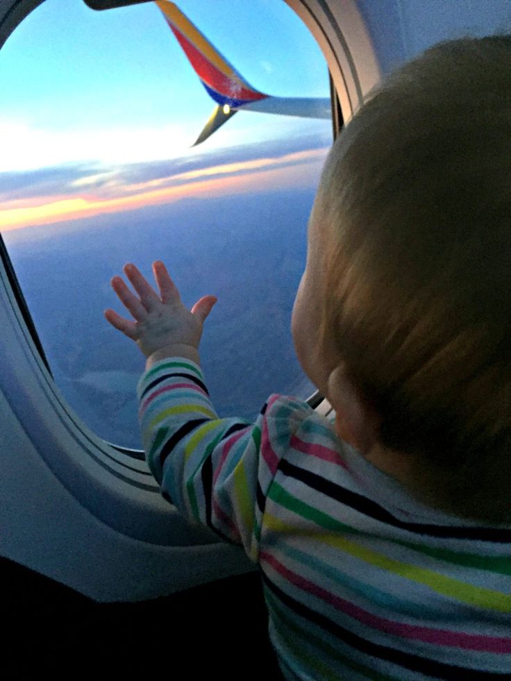 a toddler looking out an airplane window at the sunset or sunrise with his hands in the air