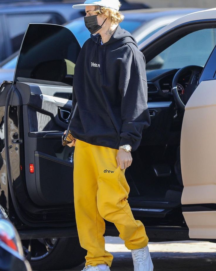 a man in yellow sweatpants and a black hoodie is stepping out of his car