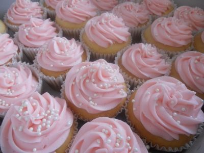 many cupcakes with pink frosting and green leaves on the top are arranged in rows