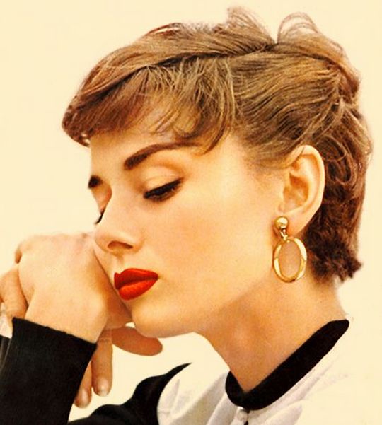 a woman with her hand on her chin and wearing large gold hoop earrings in front of her face