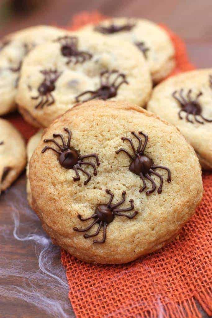 chocolate chip spider cookies on an orange cloth with text overlay that reads, chocolate chip spider cookies