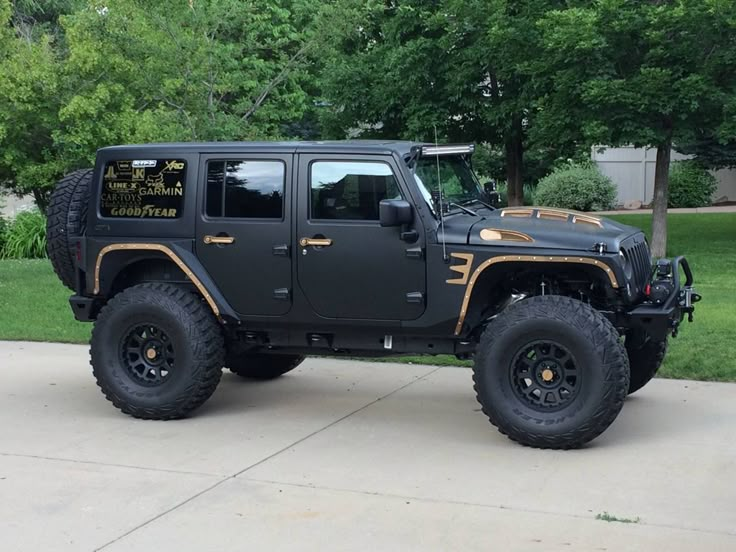 a black jeep with gold lettering parked on the side of a driveway in front of some trees