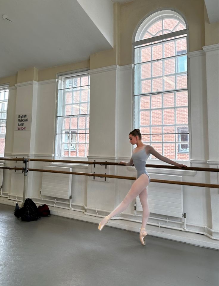 a young ballerina is practicing her moves in an empty room with two large windows