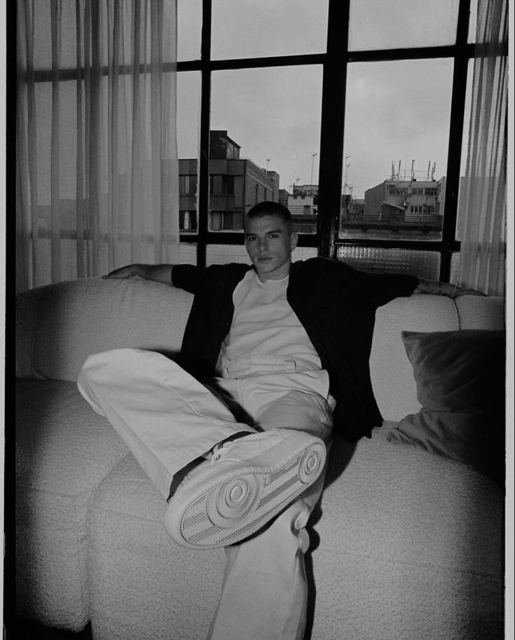 a man sitting on top of a white couch next to a window