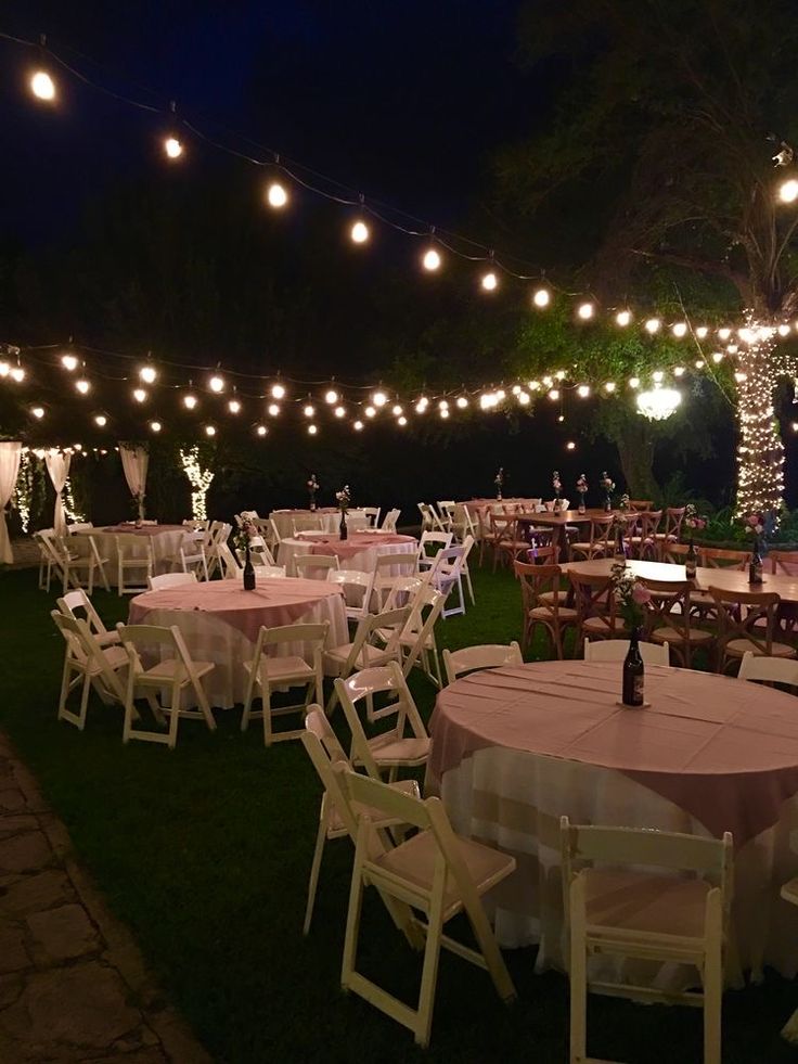 tables and chairs are set up for an outdoor event with lights strung from the ceiling