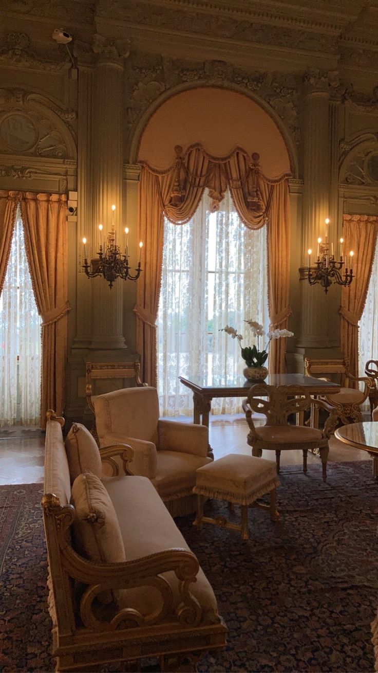 a living room with couches, chairs and chandeliers on the walls in front of large windows