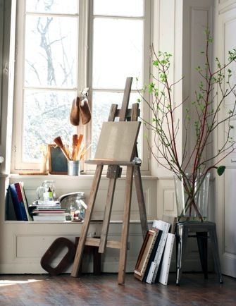 an easel sitting in front of a window next to a potted plant and books