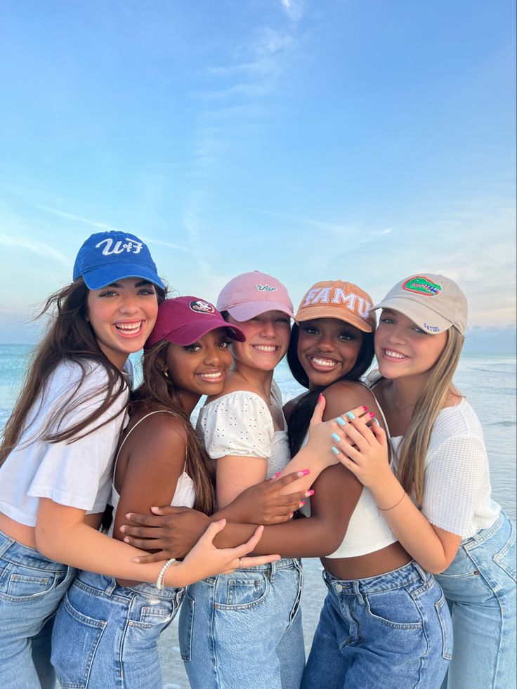 four girls standing together on the beach with their arms around each other