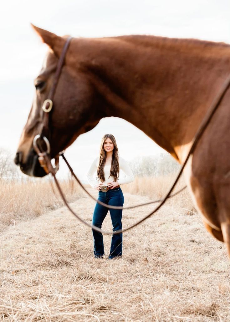 a woman standing next to a brown horse on top of a dry grass covered field