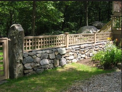 a stone wall and wooden fence in front of trees