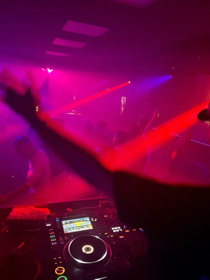 a dj mixing at a party in front of purple and red lights with his hands up