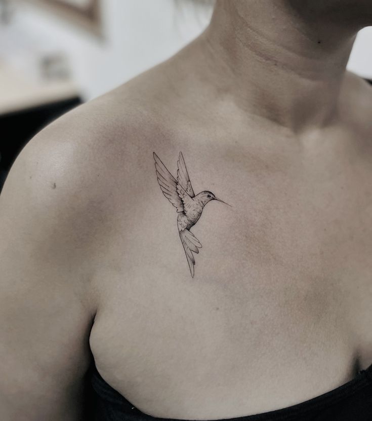 a woman's chest with a small tattoo of a hummingbird on her left shoulder