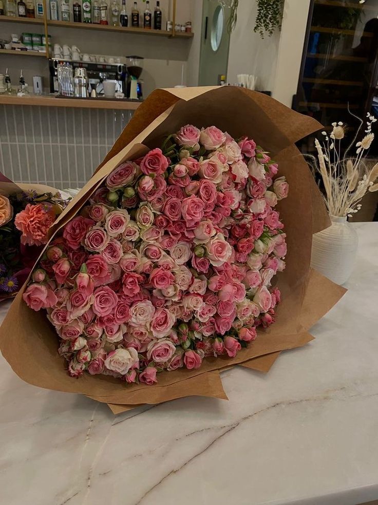 a bouquet of pink roses is wrapped in brown paper on a table with other flowers