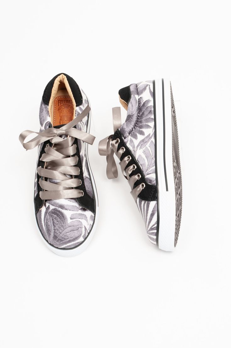 Seeking quiet luxury tones in a sneaker? Our Stormi features HAND EMBROIDERED gray florals, contrasting black trim, and luxurious silver ribbons. Our cushy padding with ample arch support sits atop a comfortable 1" sole.  Each handmade fabric is unique with different design placement. No 2 shoes are identical, and images are for representational purposes only. Whimsical Shoes, Tie Sneakers, Colorful Sneakers, Grey Ribbon, Colorful Shoes, Trending Sneakers, Quiet Luxury, Eco Friendly Fashion, Unisex Shoes