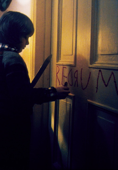 a young boy holding a large pair of scissors in front of a door with writing on it