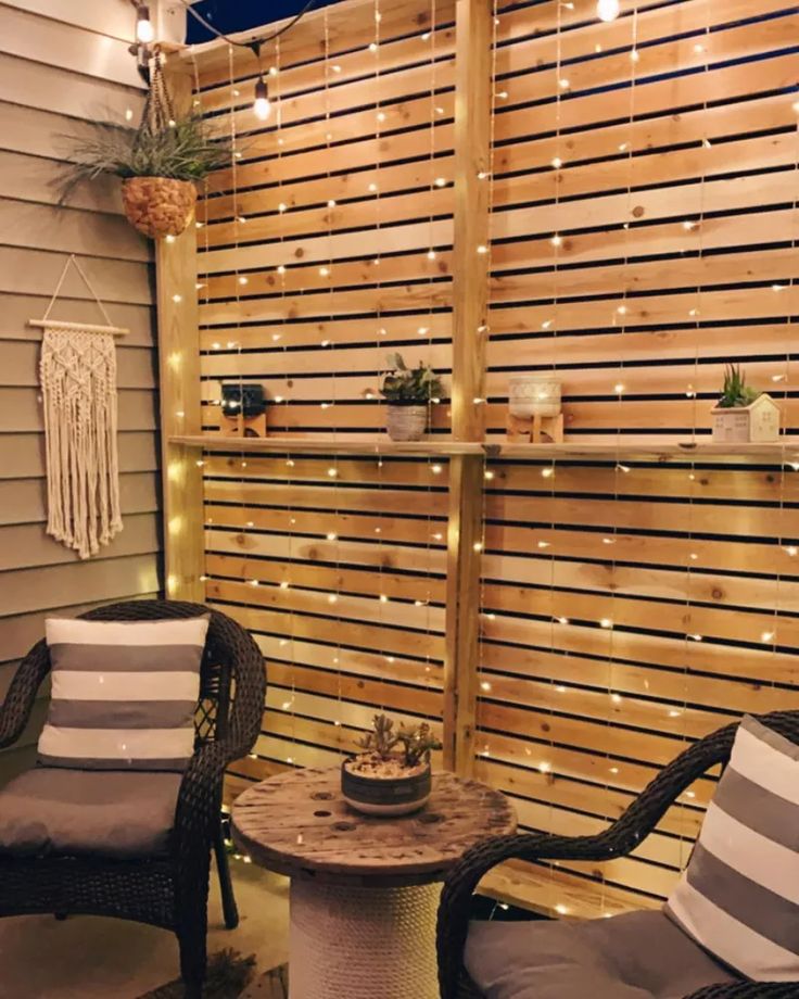 two chairs sitting next to each other near a wooden fence with string lights on it