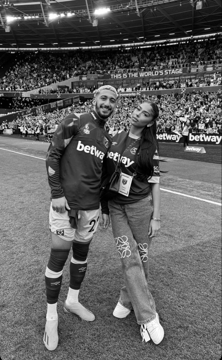 a man and woman standing next to each other in front of a stadium full of people