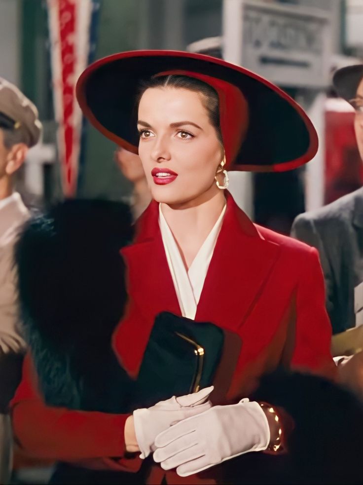 a woman in a red coat and hat with other people around her looking at the camera