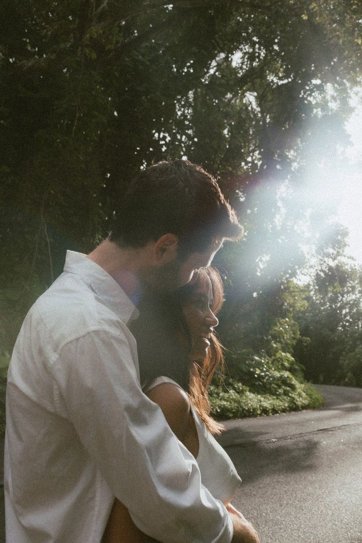 a man and woman standing next to each other on the street in front of trees