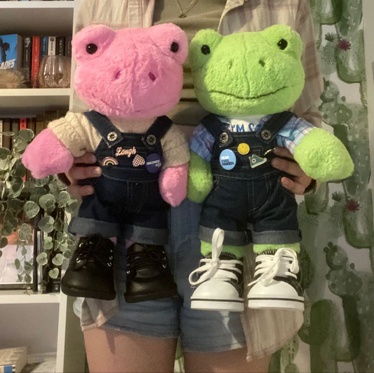 two stuffed animals that are wearing overalls next to each other in front of a bookshelf