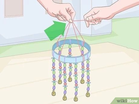 two hands are holding a small blue and green beaded wind chime hanging from the ceiling