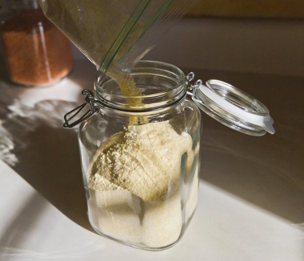 a glass jar filled with white sand next to a container full of brown stuff on top of a table