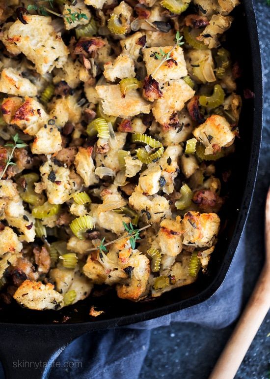 a pan filled with stuffing and vegetables on top of a blue cloth next to a wooden spoon