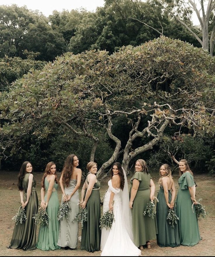 a group of women standing next to each other in front of a tree with greenery