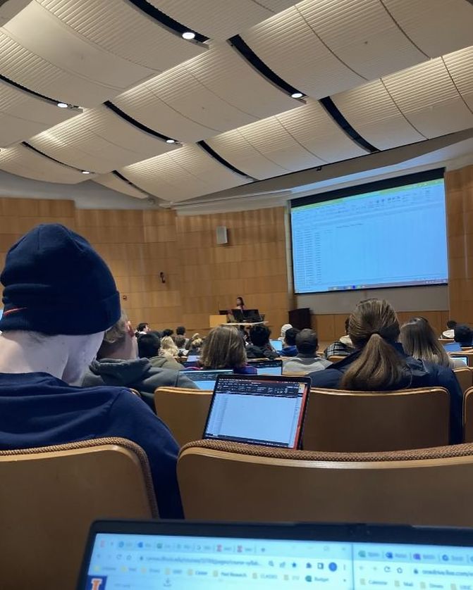 people are sitting in chairs with laptops on their laps and watching a lecture screen