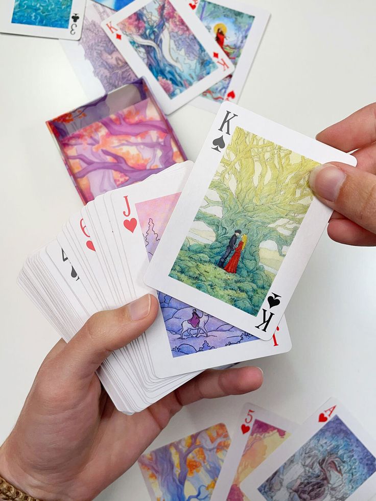 a person is holding playing cards in their hand and there are many pictures on the table