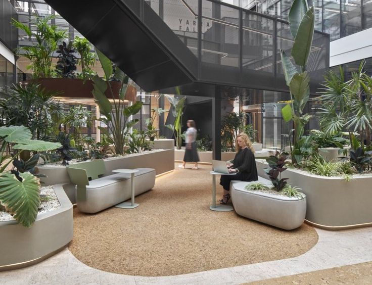 a woman sitting on a bench in the middle of an indoor area with plants and potted plants