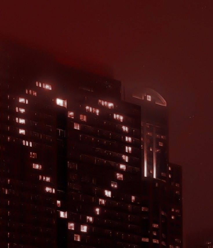 the building is lit up at night with lights on it's windows and some buildings in the background