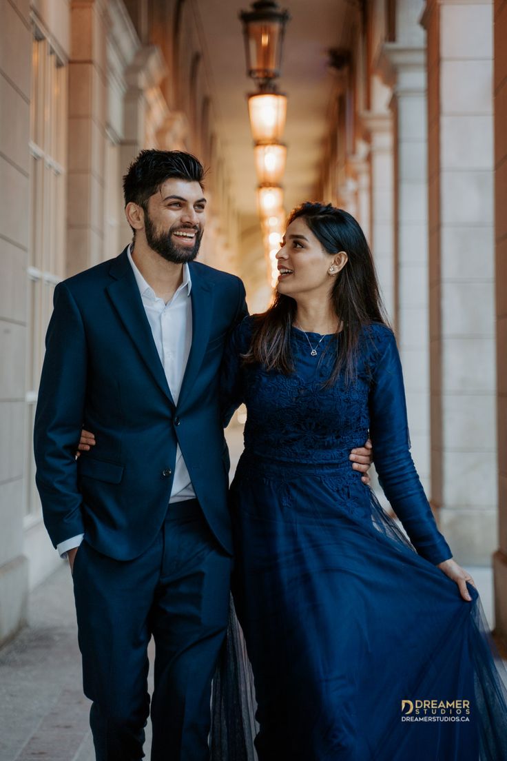 a man and woman are walking down an alley way in formal wear, smiling at each other