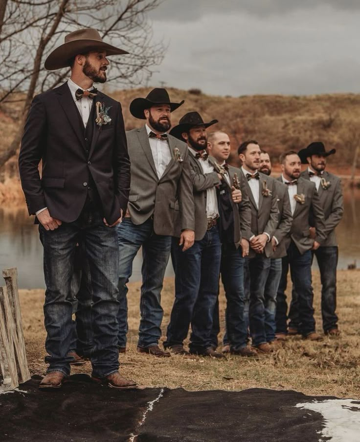 a group of men standing next to each other in front of a lake wearing cowboy hats