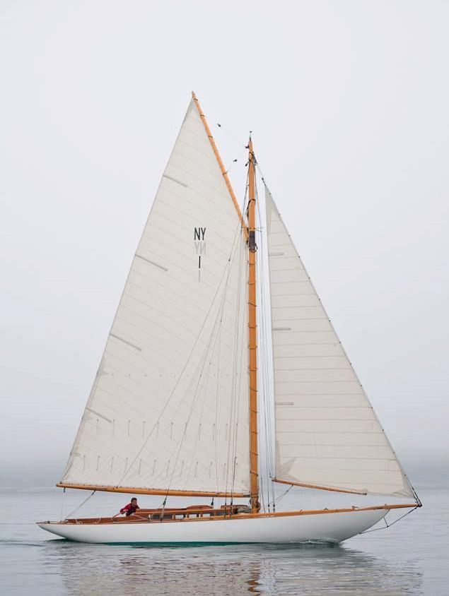 a sailboat with white sails in the ocean on a foggy day by itself