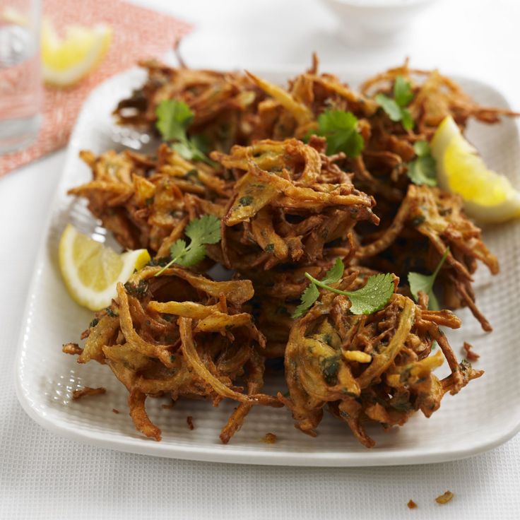 some fried food on a white plate with lemon wedges and cilantro leaves