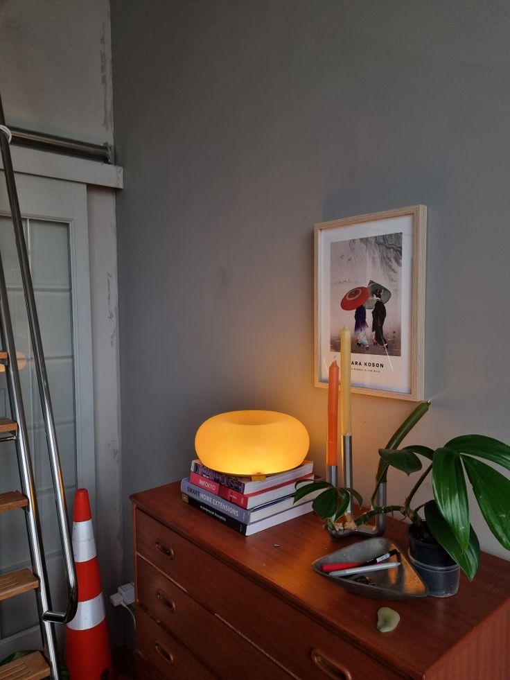 a lamp on top of a wooden dresser next to a ladder and bookshelf