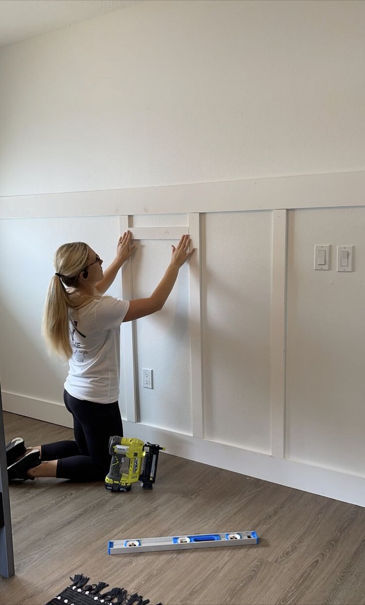 a woman is working on the wall in her room with some paint and tools nearby