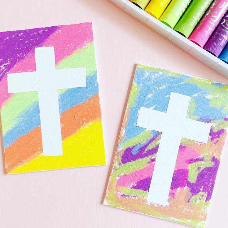 two paper cutouts with white crosses on them next to crayons