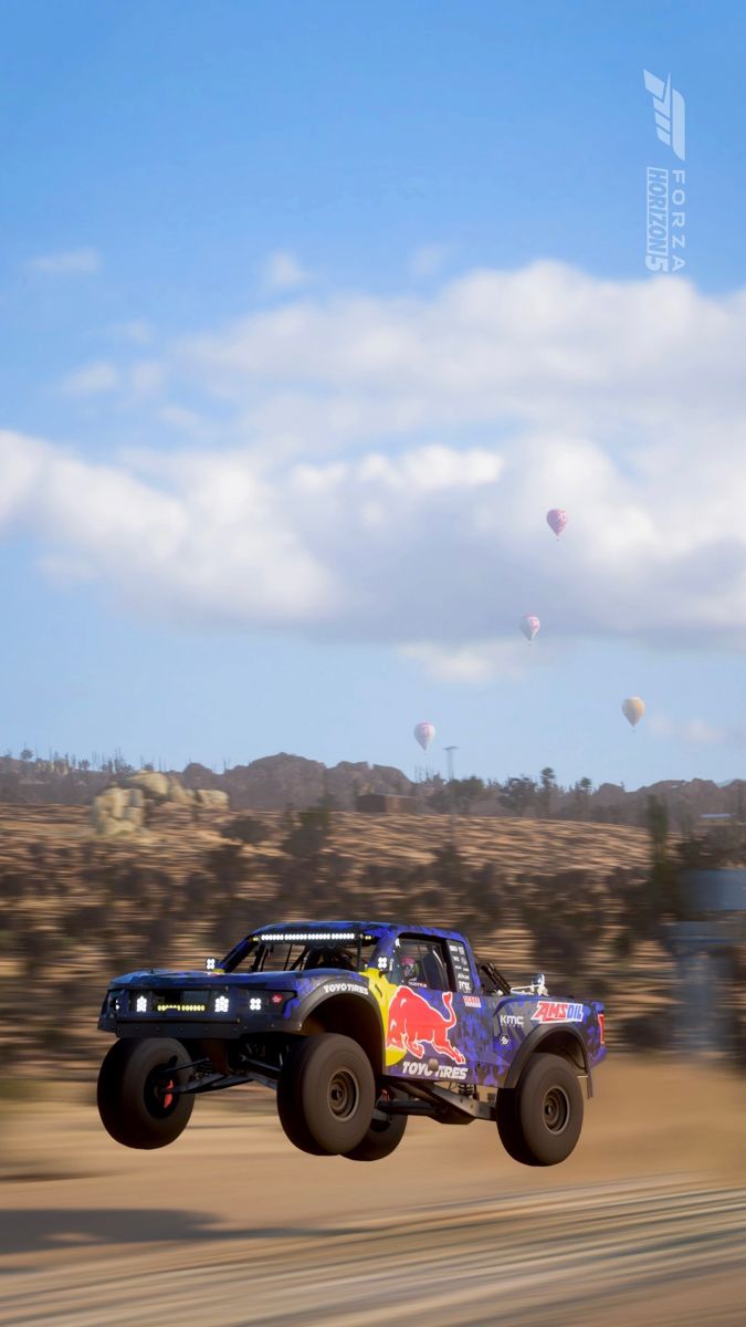 a monster truck is flying through the air with hot air balloons in the sky behind it