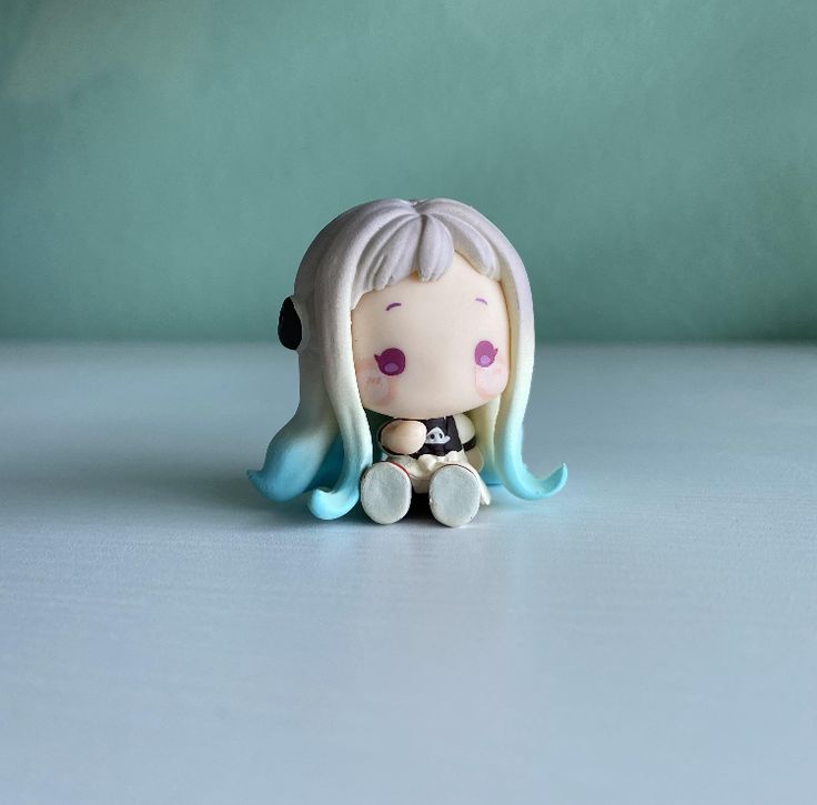 a little doll sitting on top of a table next to a blue wall and green background