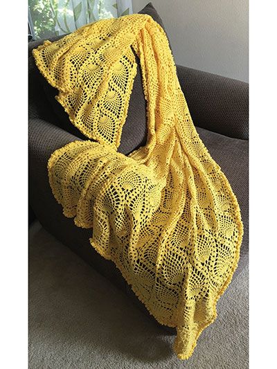 a yellow crocheted blanket sitting on top of a couch next to a window