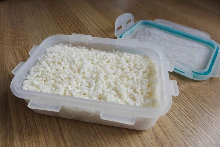 rice is in a plastic container on a wooden table next to another container with it's lid open