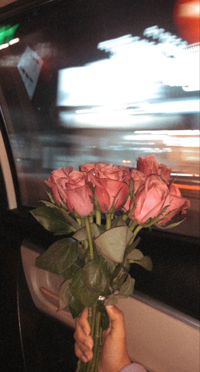 a person holding roses in their hand while sitting inside a car on the road at night