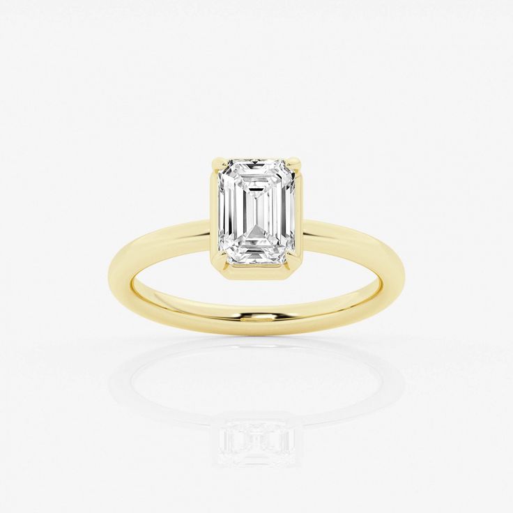 a yellow gold ring with an emerald cut diamond in the center, on a white background