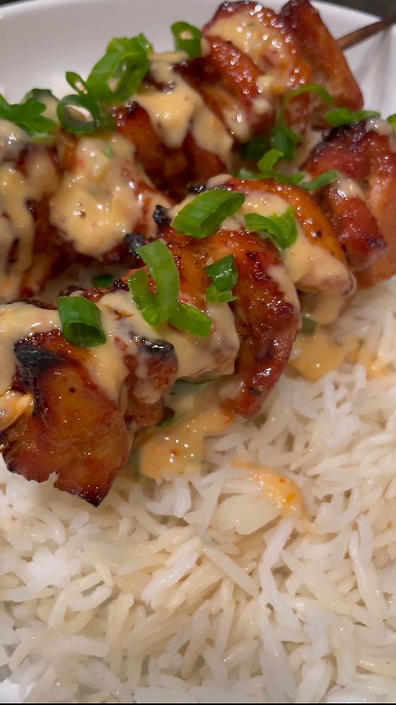 chicken skewers with sauce on top of rice and garnished with green onions