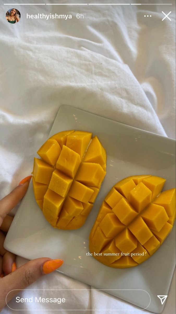 two pieces of mango on a plate with white sheets in the background and someone's hand holding an orange manicure