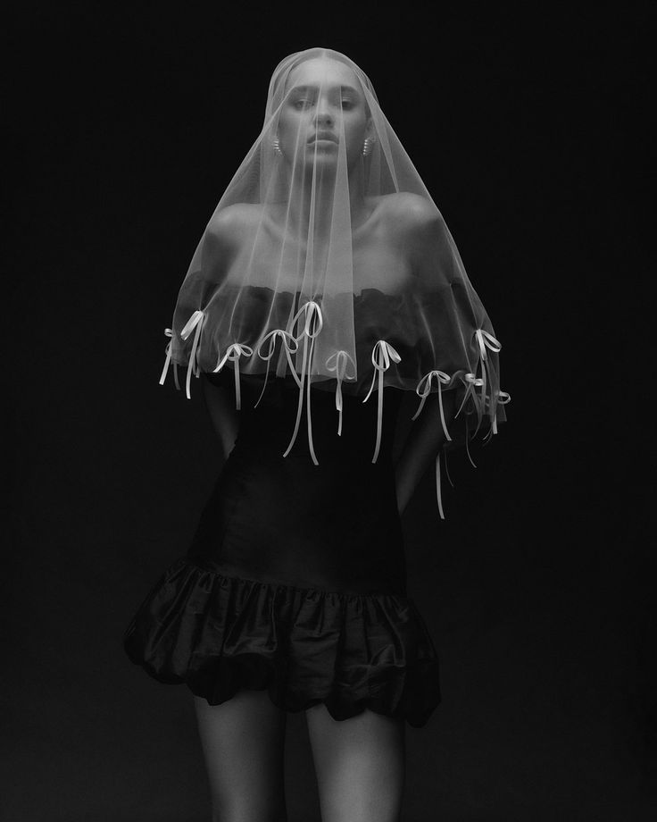 a woman with a veil on her head wearing a black dress and white shoes is standing in front of a dark background