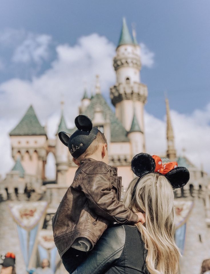 a woman holding a child in front of a castle with mickey mouse ears on it